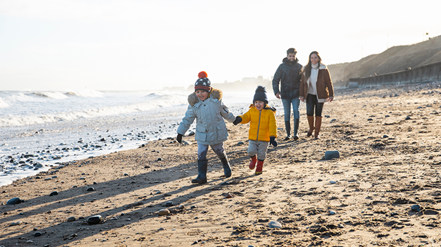 A multi-generation family wrapped up in warm clothing on the beach on a cold day in January.